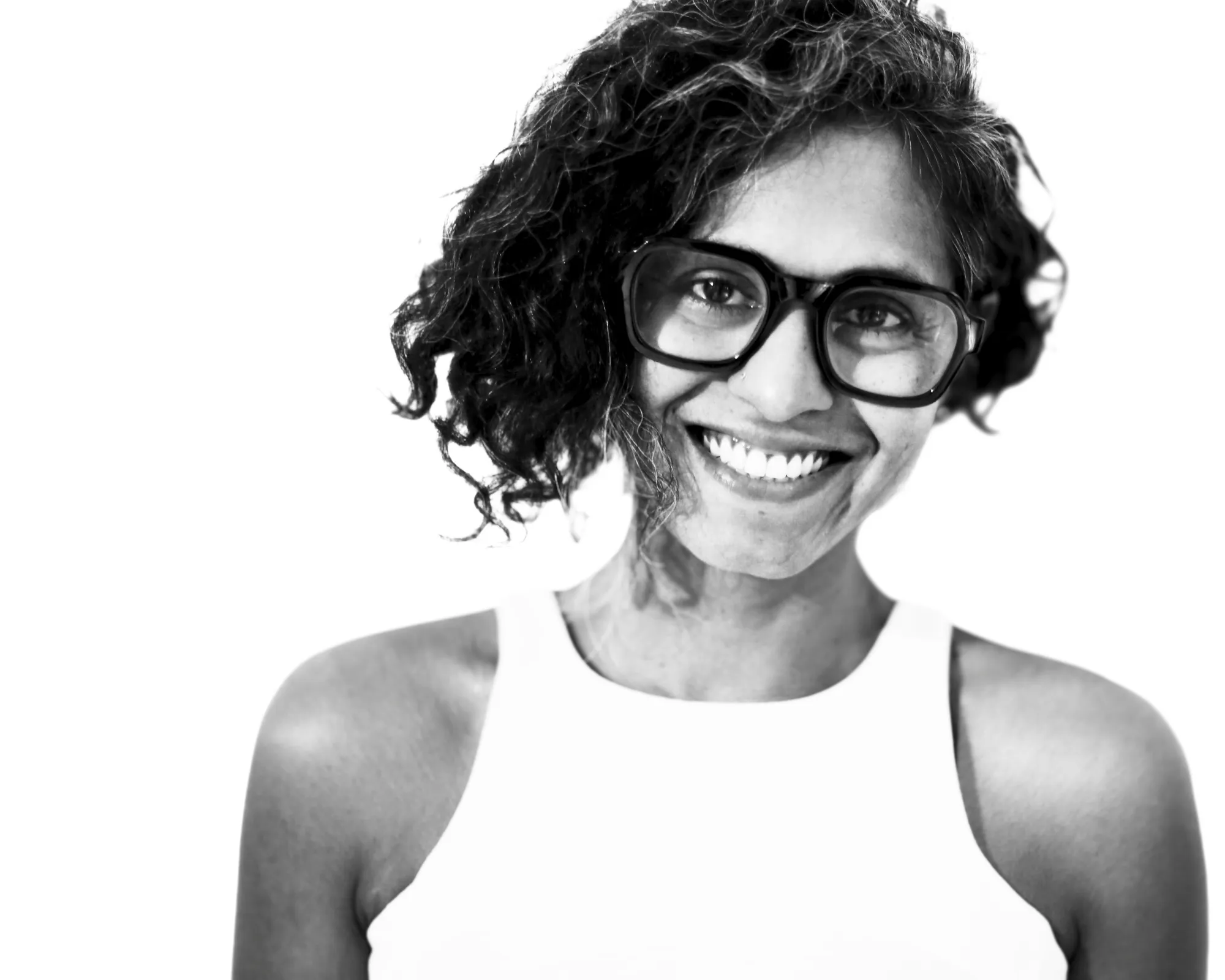 Shilpa, a woman, wearing glasses in a sleeveless top is looking into camera smiling.